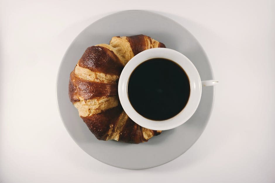 A cappuccino and a croissant served on a white plate