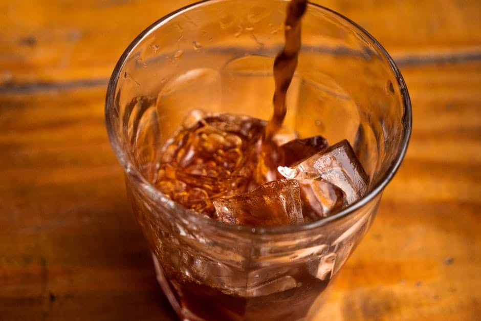 Coarsely ground coffee beans next to a glass of cold brew coffee with ice