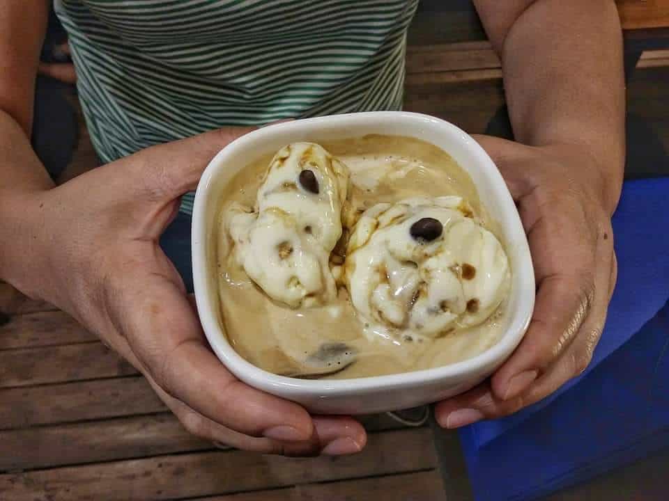 A scoop of vanilla ice cream in a glass bowl with cold brew coffee being poured over it to make an affogato