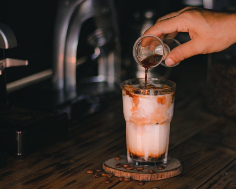 Overhead view of coarsely ground coffee being poured into a large glass jar filled with water to make cold brew